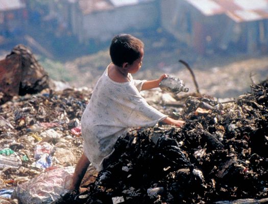 A young child digs through a pile of trash in a landfill