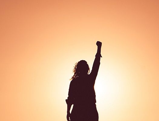The sun sets on a woman holding a fist in the air