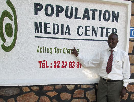 Jean Bosco points to the Population Media Center sign in Burundi