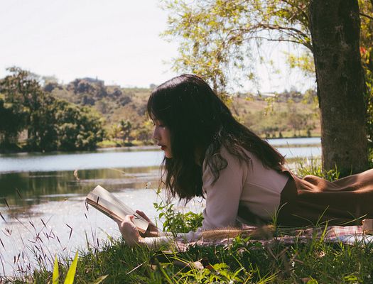 A woman reads a book by a river
