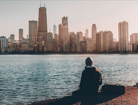A man sits on the edge of a lake while looking at the a skyline