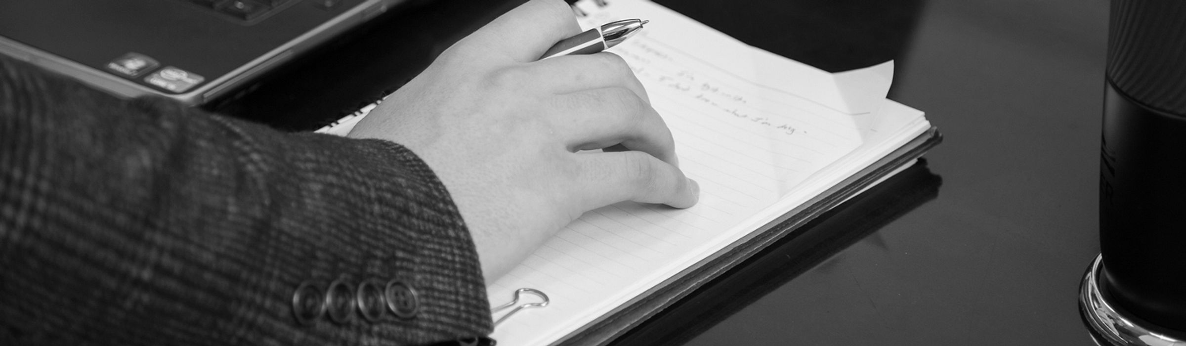 A person holding a pen resting their hand on a notebook